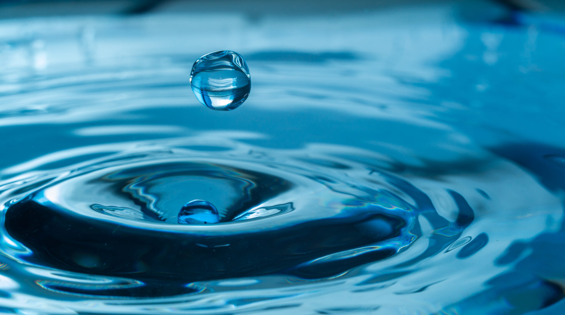 A water drop falling into the ocean with a blue background.